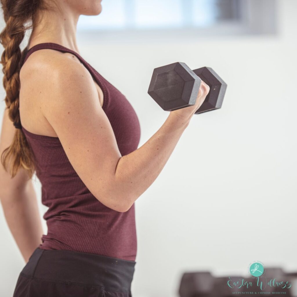 A woman performing a bicep curl with a dumbbell, highlighting the importance of strength training to maintain muscle mass and support kidney Qi in TCM.